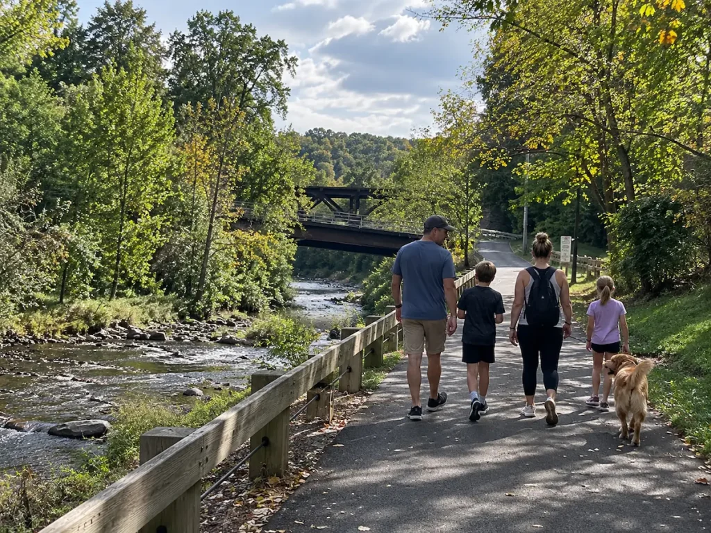 A family walking a paved creekside greenway trail with their dog
